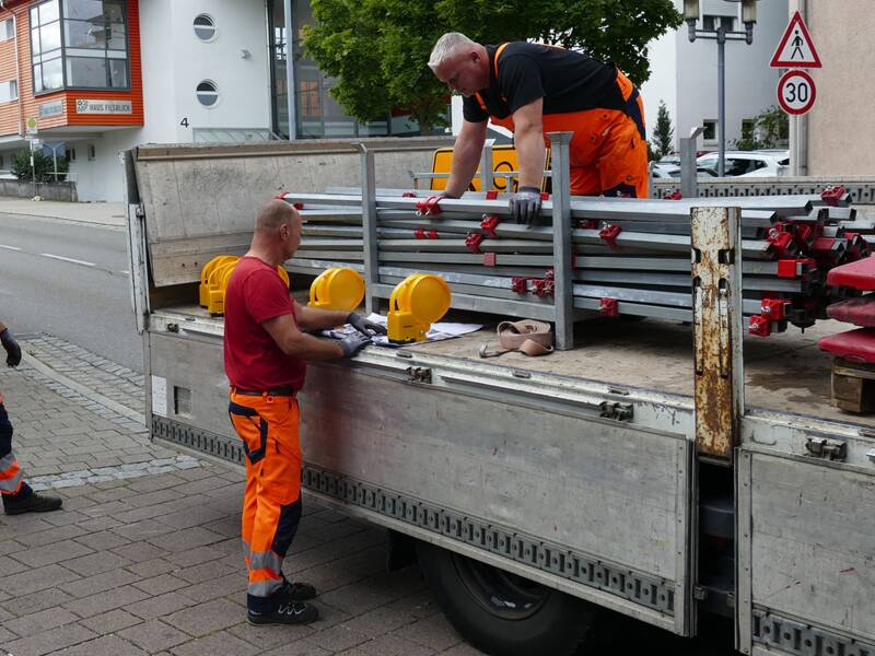 Bauarbeiter beim Einrichten einer Baustelle in Ebersbach an der Fils auf einem Transportfahrzeug mit aufgeladenen Absperrgittern