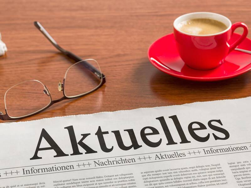 Eine Zeitung mit dem Titel Aktuelles liegt auf einem Tisch mit einer Kaffeetasse und einer Brille