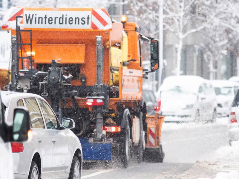 Schneepflug beim Räumen einer verschneiten Straße, gefolgt von Autos