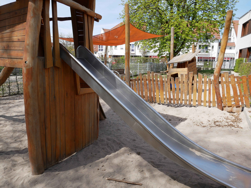  Außengelände des Kinderhaus Schatzkiste mit Rutsche im Vordergrund auf einem sandigen Untergrund