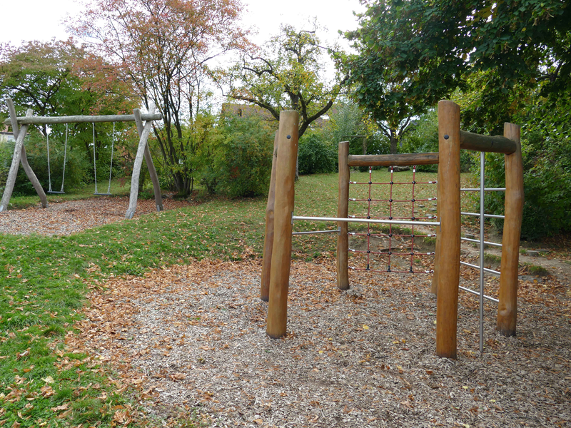 Außengelände des Kindergarten Unterm Regen Sulpach mit einem Schaukelgestell aus Holz und zwei Schaukeln sowie einem sechseckigen Holzelement mit verschiedenen Kletter- und Turnmöglichkeiten