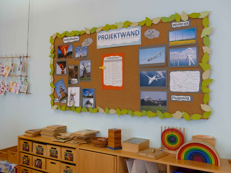 Projektwand mit Bildern zu verschiedenen Themen über Holzschränken mit Holzspielzeug im Kindergarten Unterm Regen Sulpach