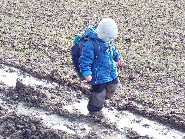 Warm angezogenes Kind des Fuchskinder Naturkindergarten Roßwälden bei einem Spaziergang in einer Matschpfütze