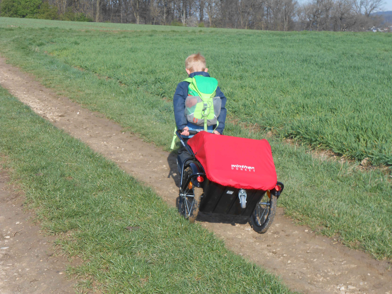 Ein Kind des Rotmilane Naturkindergarten Weiler zieht einen kleinen Transportwagen bei einem Ausflug in der Natur auf einem Feldweg 