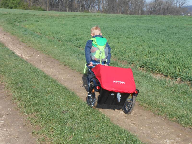 Ein Kind des Rotmilane Naturkindergarten Weiler zieht einen kleinen Transportwagen bei einem Ausflug in der Natur auf einem Feldweg 
