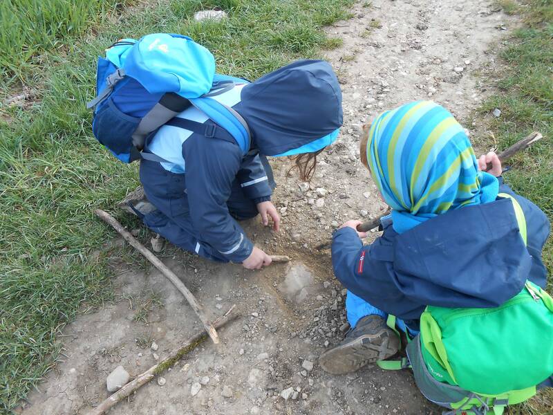 Kinder des Rotmilane Naturkindergarten Weiler kniehen auf einem kleinen Pfad und spielen mit Stöckern in der Erde