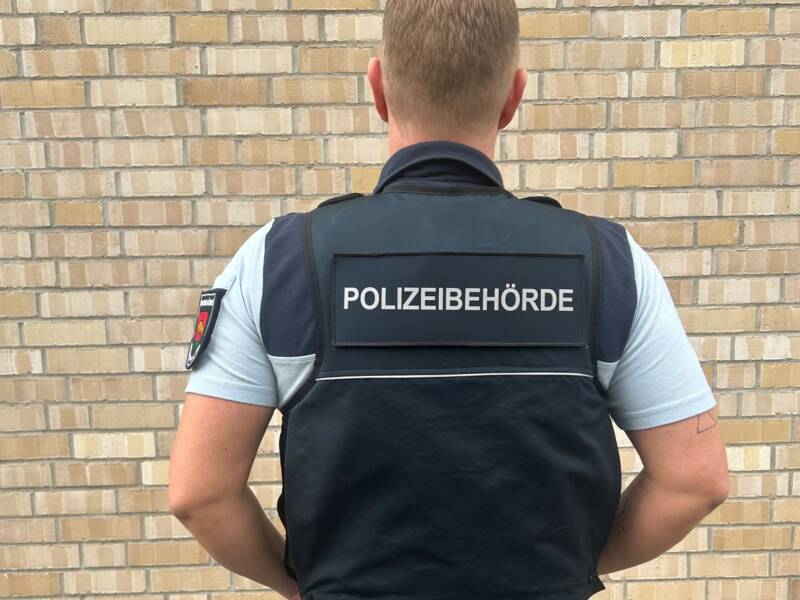 Rückansicht eines Ordnungsamt Mitarbeiters mit der neuen blauen Schutzweste mit der Aufschrift Polizeibehörde