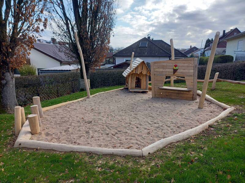 Großer Sandkasten mit einem kleinen Spielhaus aus Holz und einem Eisverkaufsstand zum Spielen aus Holz