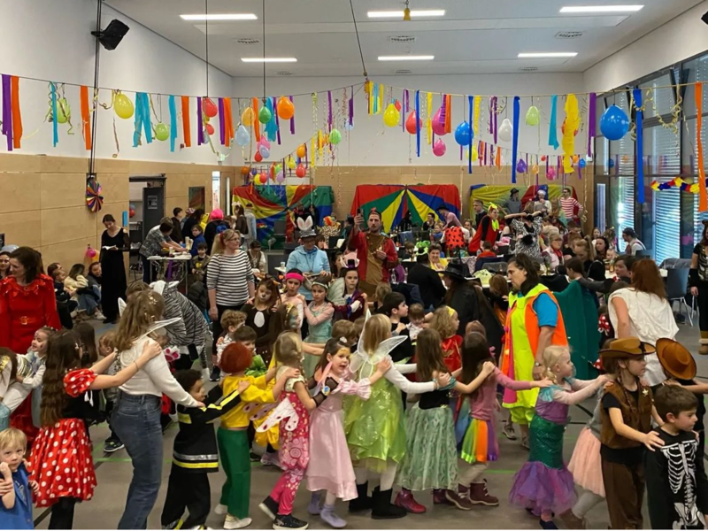 In einem bunt geschmückten Raum feiern viele Kinder in Kostümen fröhlich zusammen Karneval.